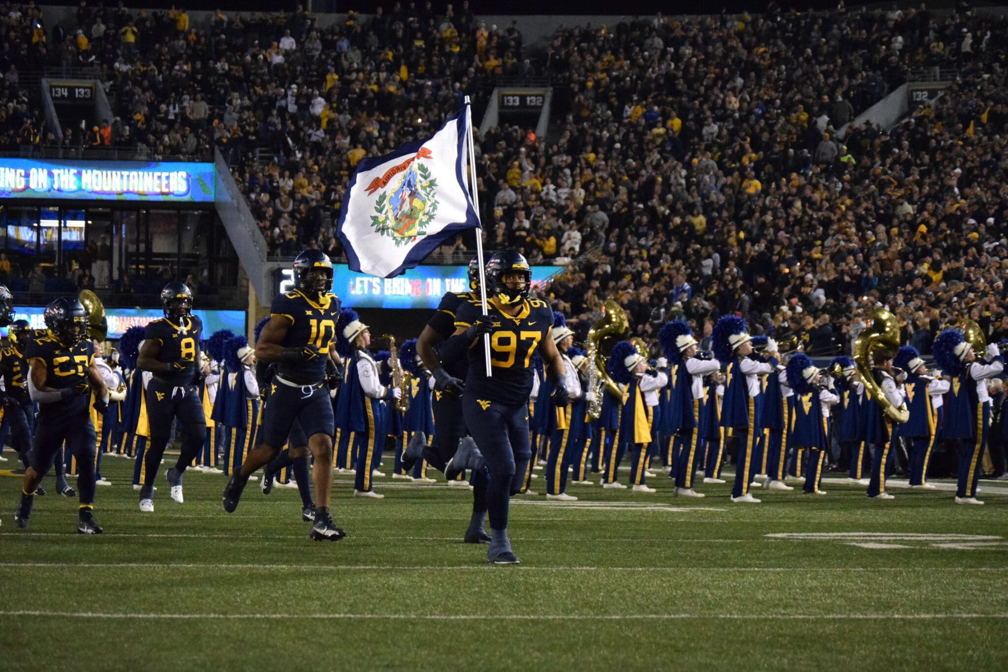 WVU Football running on field with West Virginia flag