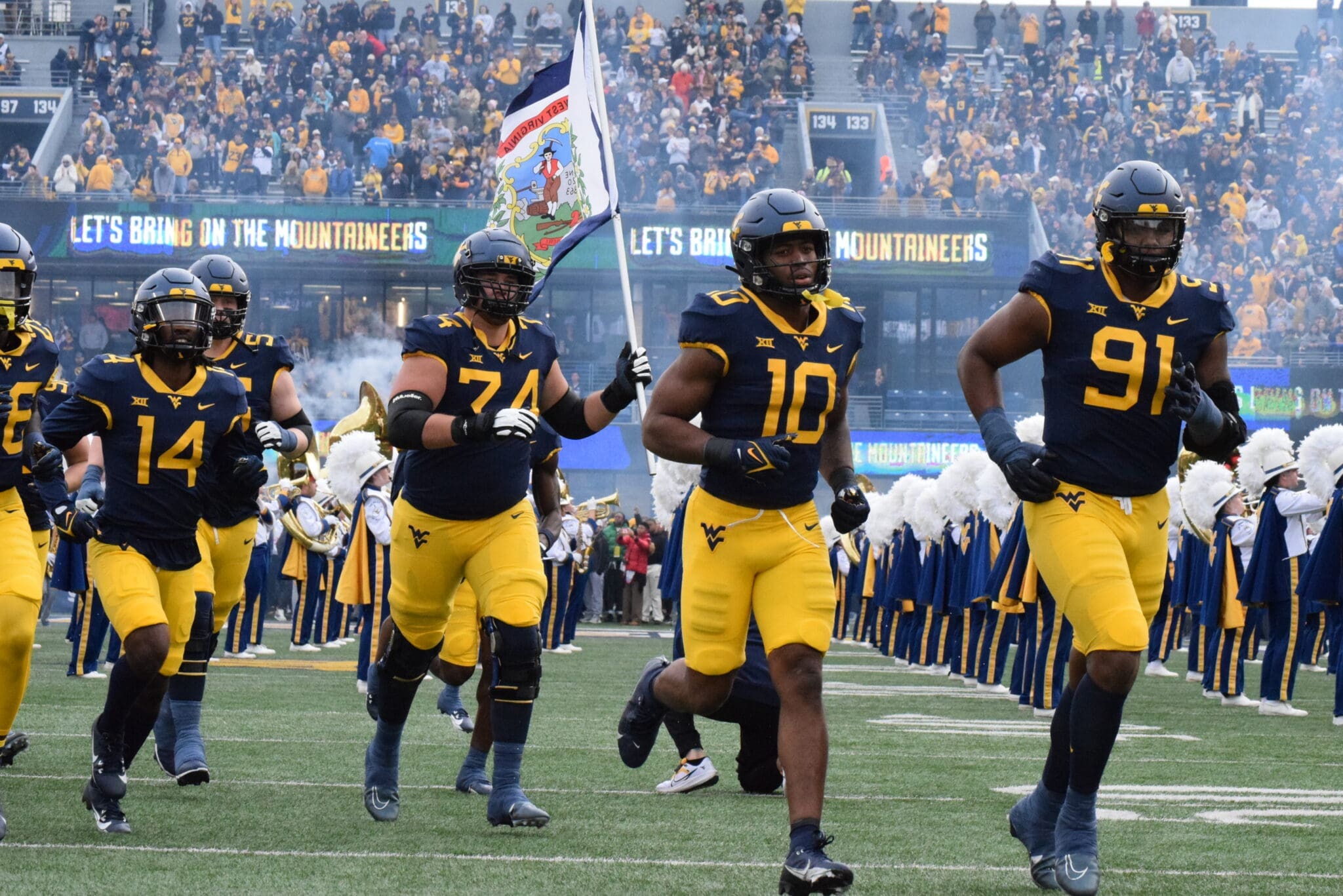WVU Football players run on field with flag, including OL Wyatt Milum